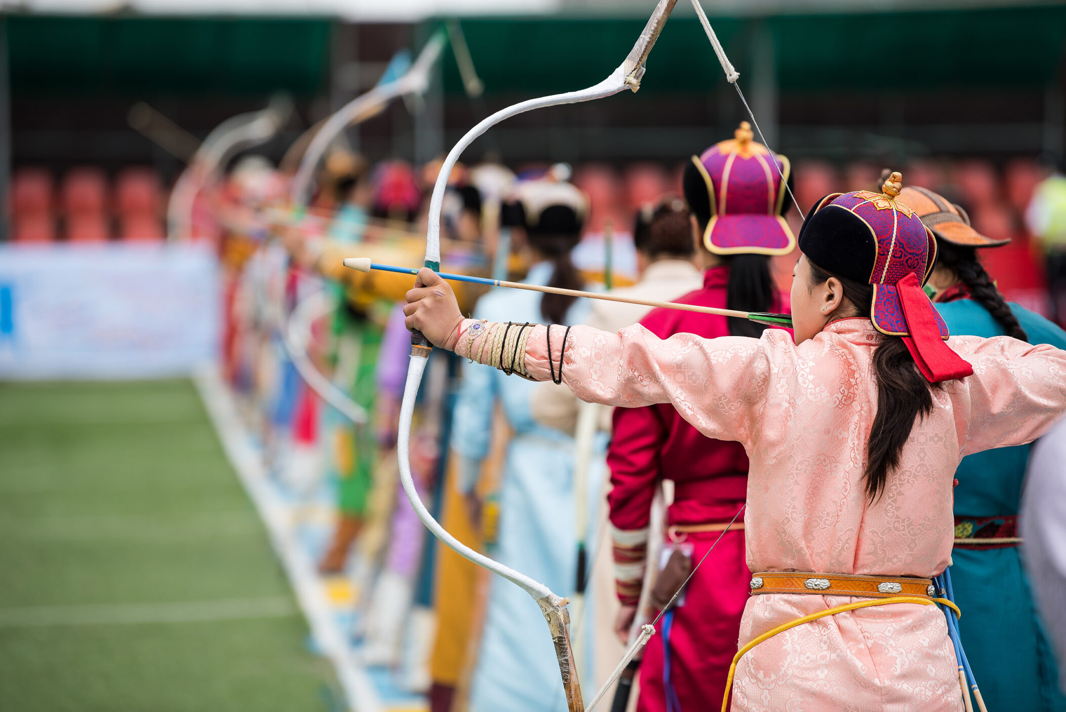 Naadam festival Mongolia archery, Mongolian women in traditional Mongolian dress shooting arrows with Mongol bow and arrow, colorful traditional costumes during Naadam competition in july