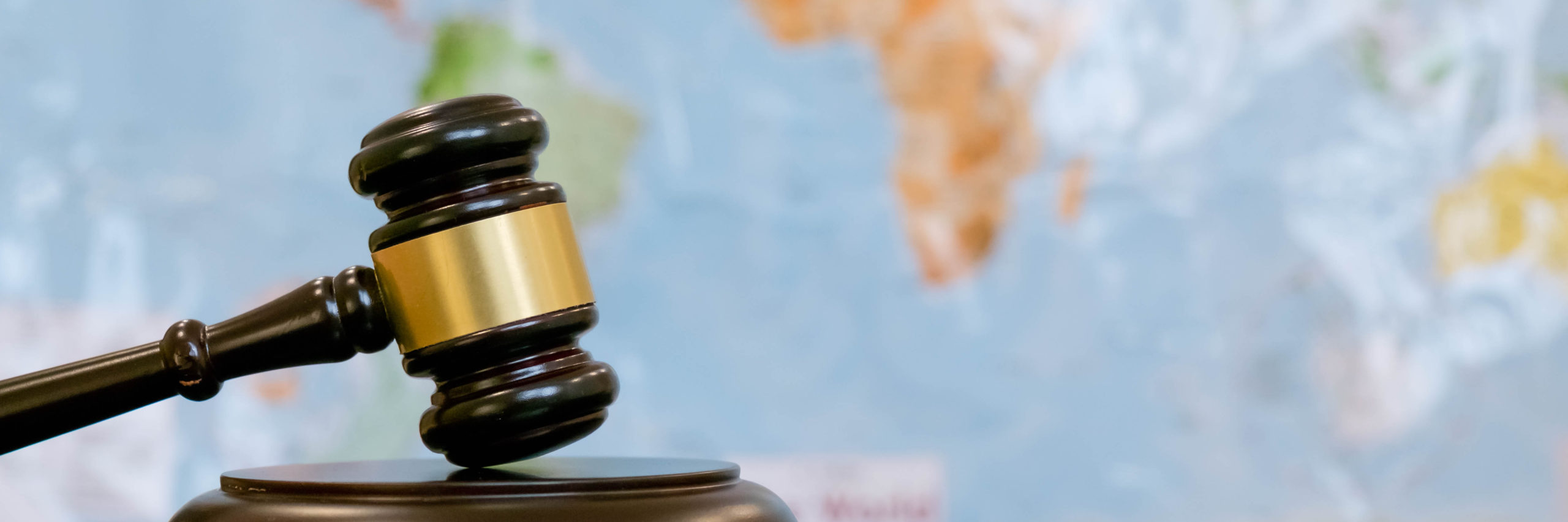 Judge's gavel and over world map. Symbol for jurisdiction. Law concept a wooden judges gavel on table in a courtroom or law enforcement office on blue background. Copy space for text - Image