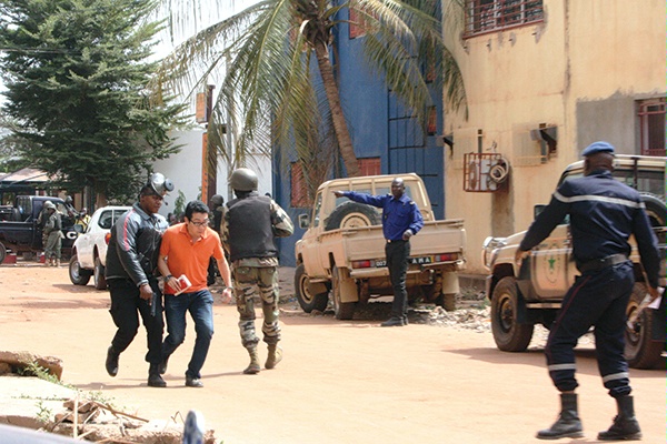 A hotel patron (in orange shirt) is evacuated to safety as Malian police and soldiers establish a perimeter around the building, November 20, 2015. (AP/Wide World Photos)