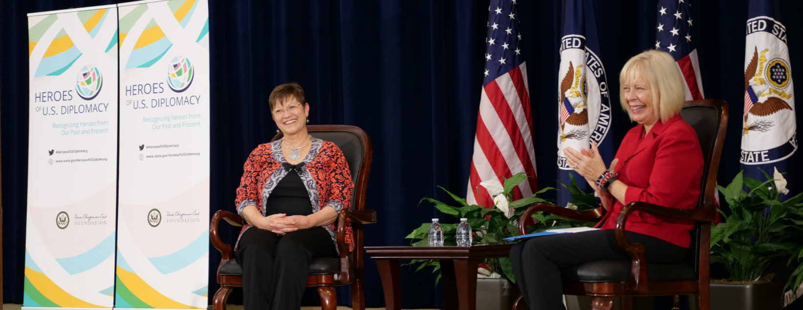 Elizabeth Slater and Director General Carol Perez sit in armchairs on the stage for the launch of the Heroes of U.S. Diplomacy initiative.