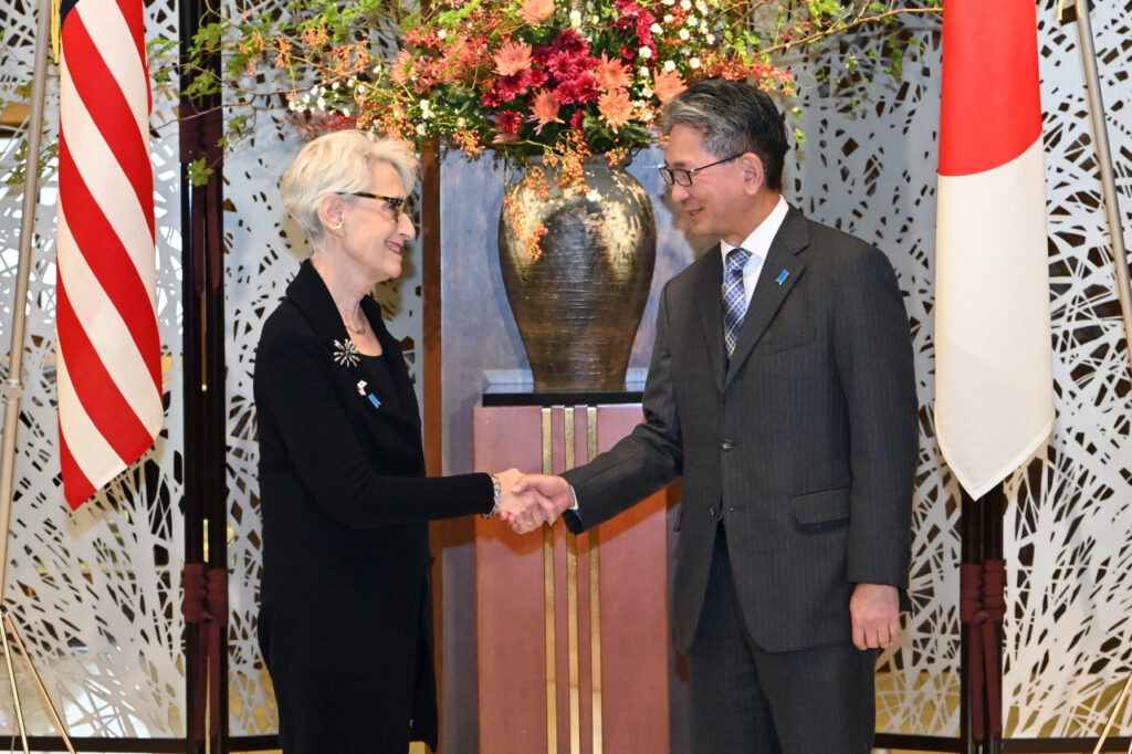 Deputy Secretary and Japanese Foreign Minister shaking hands in front of American and Japanese flags