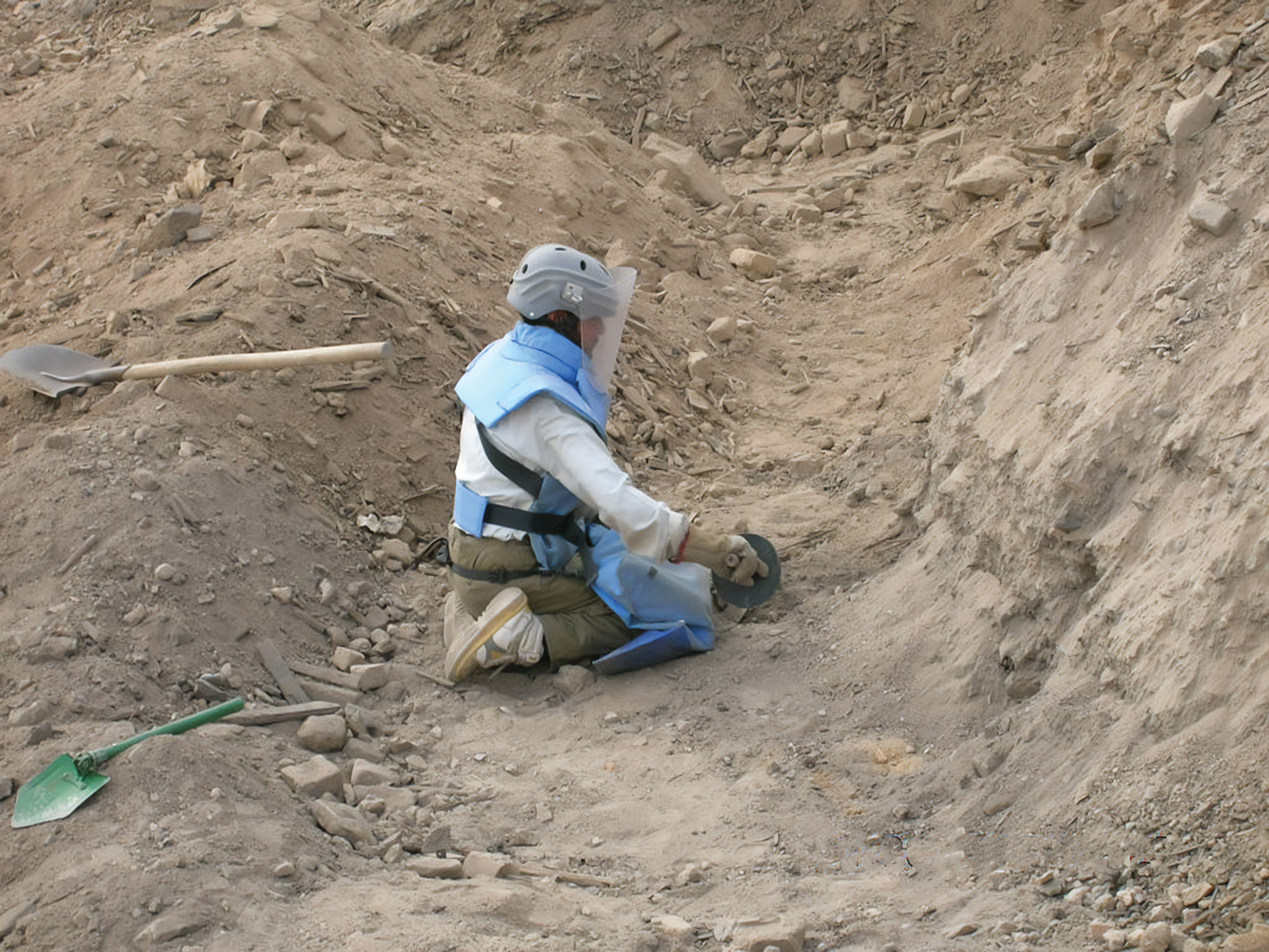 A person in protective gear kneeling in a large dirt pit