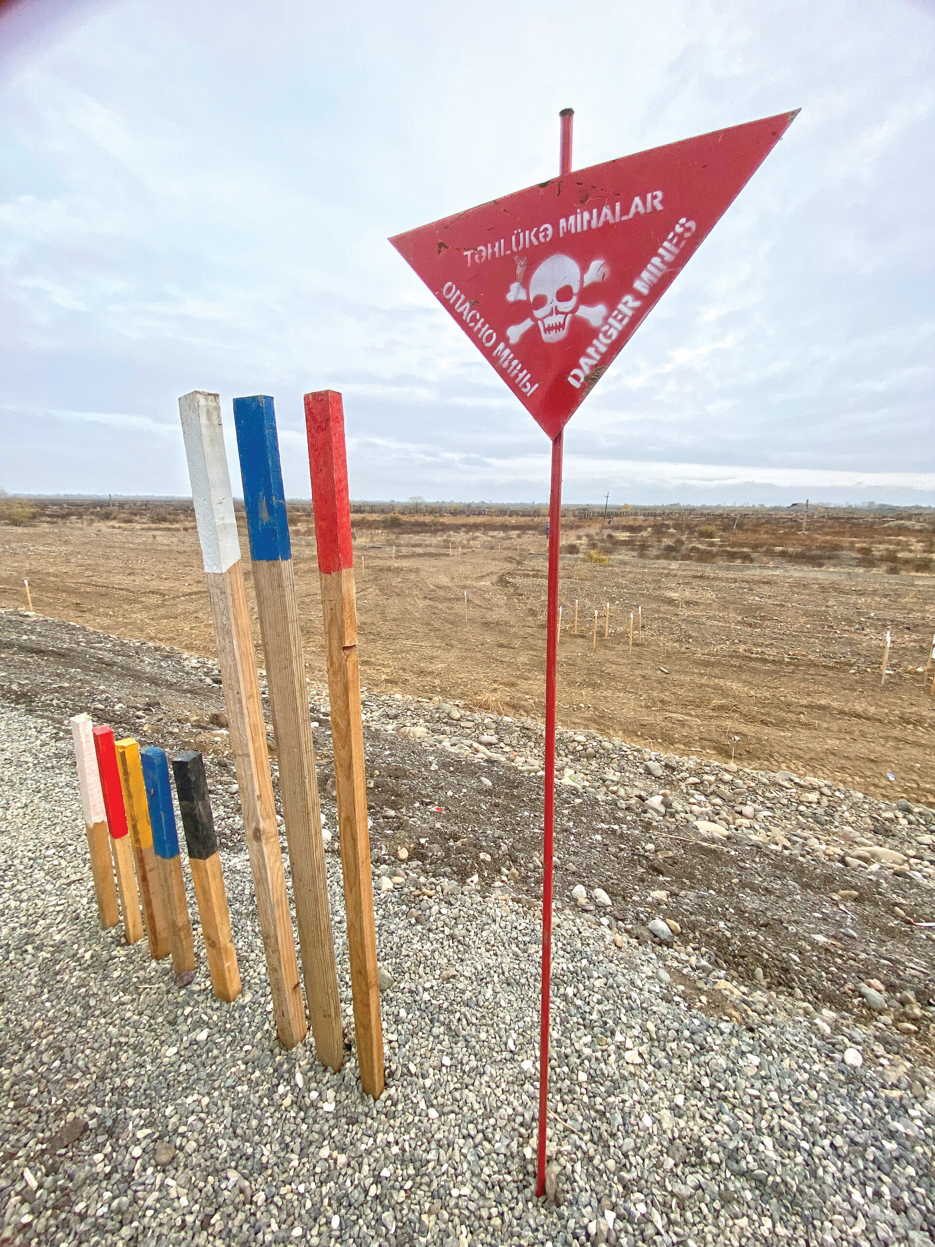 A red triangular sign with a skull and crossbones beside three stakes, one white, one blue, one red