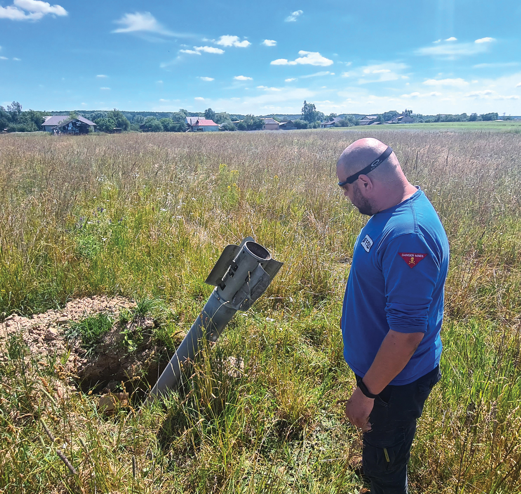 A man in a field stands next to an unexploded rocket sticking out of the ground.