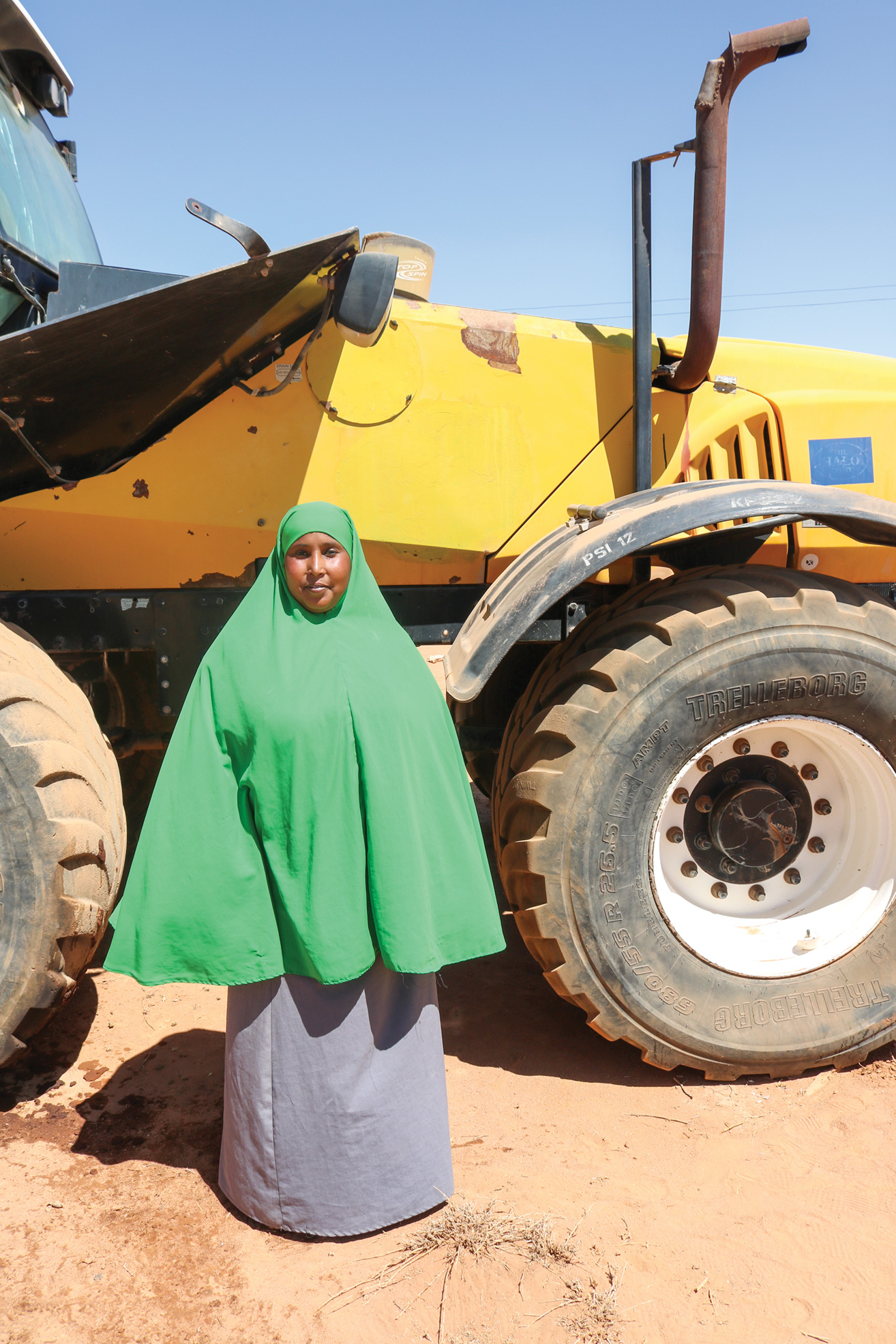 A woman stands in front of a large tractor-like piece of equipment that she operates to conduct mechanical demining