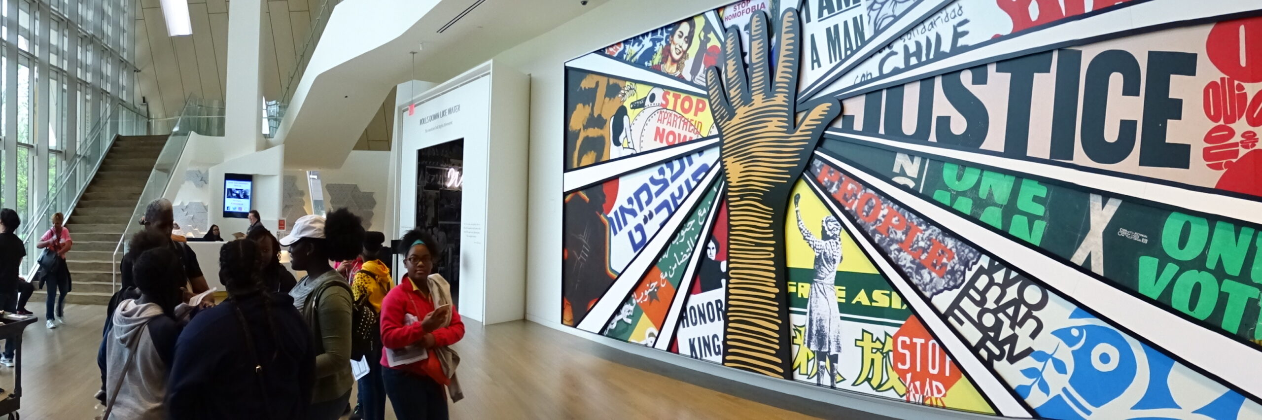 Panorama of a lobby, highlighting a mural with a hand in the center with various civil and human rights messages/images surrounding the hand.
