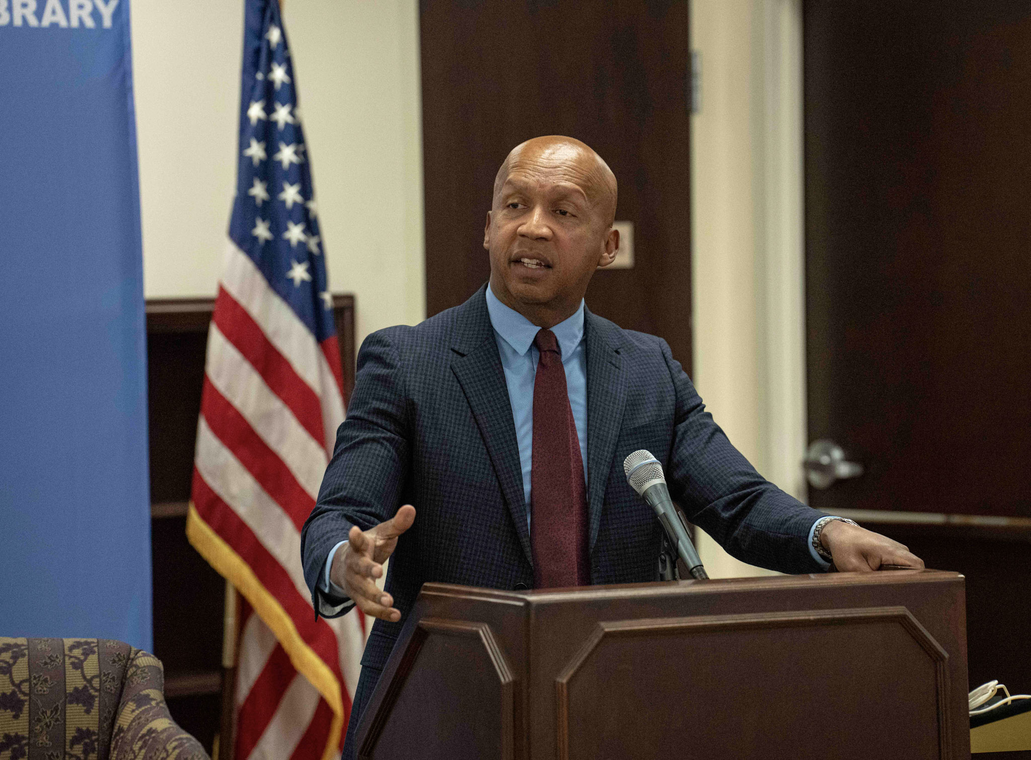 Equal Justice Initiative Executive Director Bryan Stevenson speaking at the Ralph J. Bunche State Department Library. He is standing at a lectern and a U.S. flag is behind him. [State Department photo]
